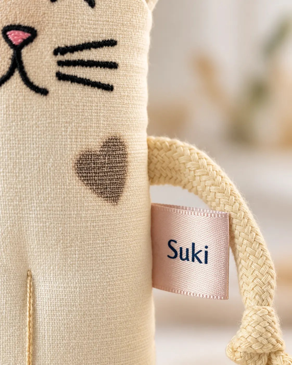 Detalhe do coração costurado no corpo de um Let’s Cats, ao lado da etiqueta com o nome do personagem